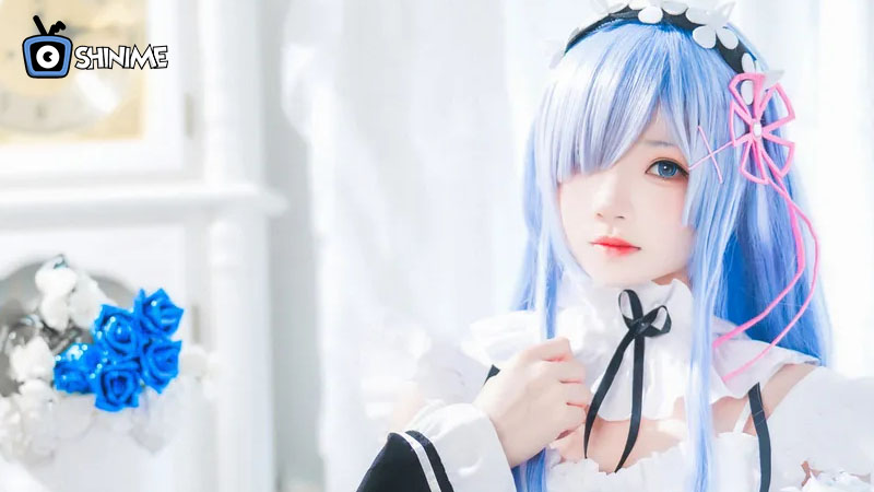 Cosplayer de Rem con peluca azul, cinta rosa y vestido de sirvienta, personaje popular para cosplay en 2025.