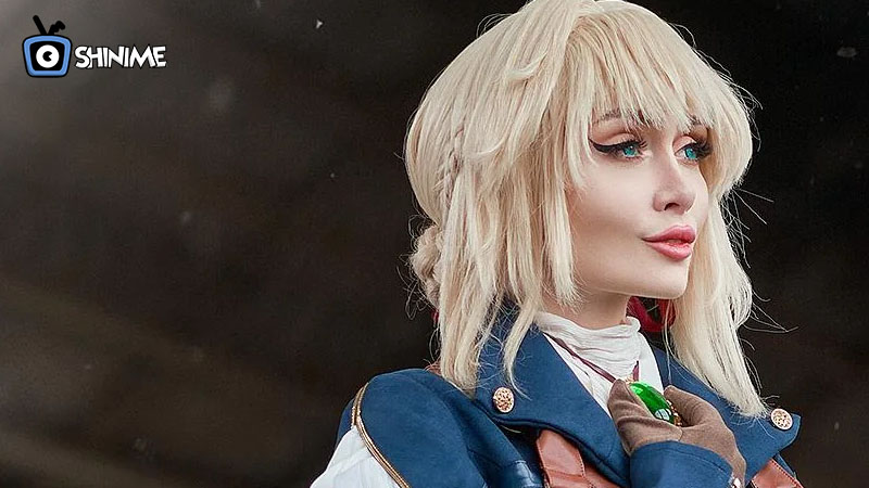 Cosplayer de Violet Evergarden con uniforme azul y broche, elegancia emocional entre cosplays populares.